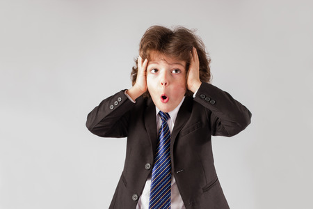 Little curly boy grabbed his hands behind his head and his mouth open in surprise looking up. Gray background.の写真素材