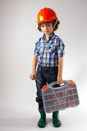 Little curly-haired worker in a helmet with a box. Gray background.の写真素材