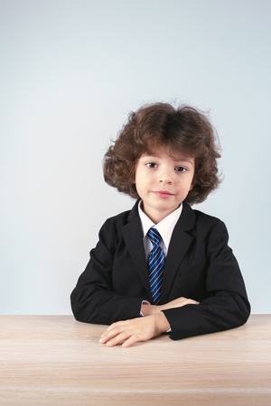 Cute little businessman sitting at the table. Gray background.の写真素材