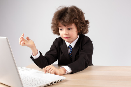 Clever little businessman working with laptop. Gray background.の写真素材