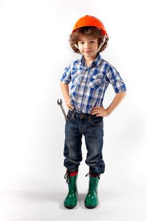 Little curly-haired worker in an orange helmet with a key in his pocket. Gray background.の写真素材