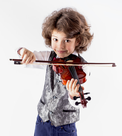 Cute curly-haired boy in a waistcoat playing the violin leaning forward. Close-up. Gray background.の写真素材