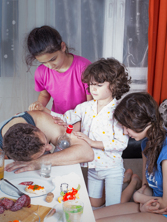 Three children are sad drunk had fallen asleep near the table father. On the table are drink and snack.の写真素材