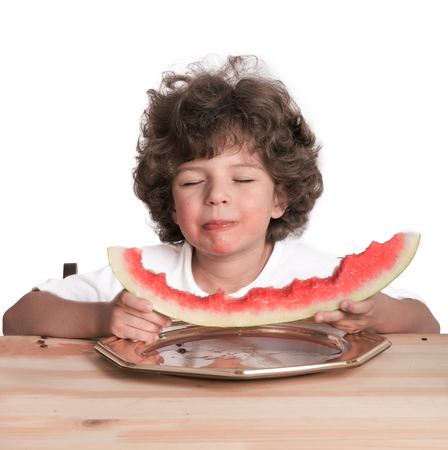 Small happy little boy covering his eyes with pleasure eat delicious ripe watermelon. White background. Close-up.の写真素材