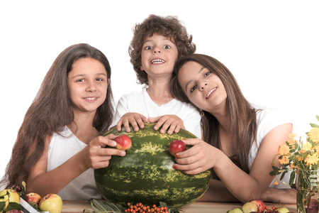 Happy family with a whole watermelon and apples on a white background. Sitting at the table. Looking at the camera. Close-up.の写真素材