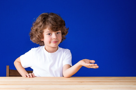 Happy curly cute boy points his hand forward and looking at the camera. Close-up. Blue background.の写真素材