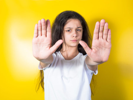 Young woman making a stop sign. Yellow background
