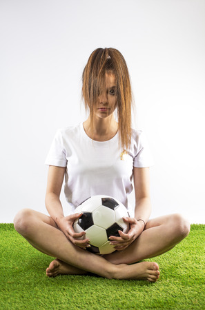 Elegant teenager with Football ball sits on the grass. Smart soccer player. Gray background.の写真素材