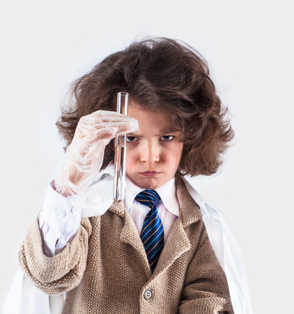 Little curly-haired boy scientist looks at test tube with clear liquid. Gray background