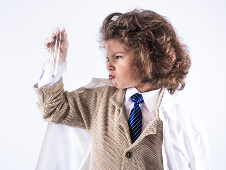 A ilittle curly-haired boy in a medical gown holds a test tube with one hand . White background.の写真素材