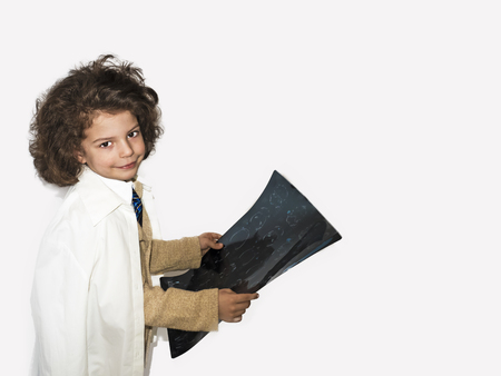 Smart curly-haired boy in a lab coat holding x-ray isolated on gray backgroundの写真素材