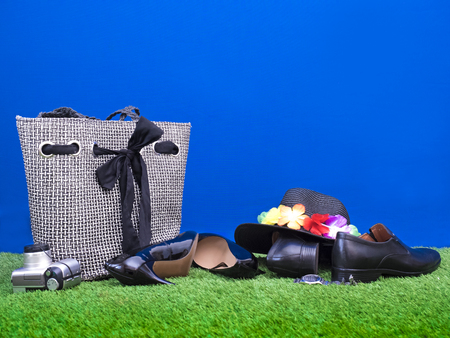 Beach bag, business shoes, camera, hat, clock lie on the grass on a blue with space for text or image. Rest conceptの写真素材