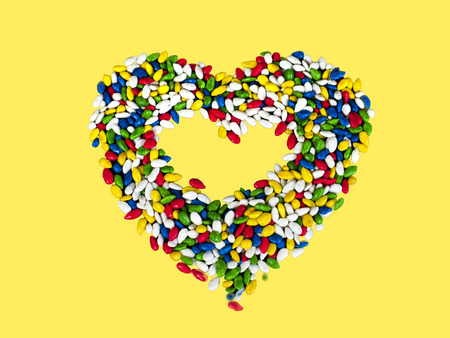 Sweets in heart shaped. Sunflower seeds in color glaze. Yellow backgroundの写真素材