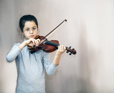 A thoughtful girl with spectacles plays the violin.の写真素材