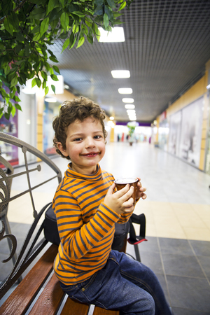 A little boy with his mouth smeared coffe sits on the bench and looking at the cameraの写真素材