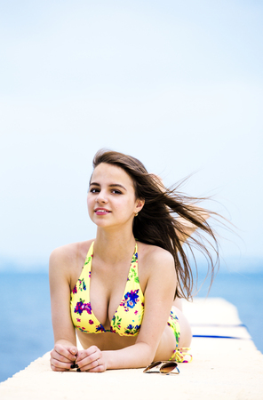 Relaxing young woman on pier at the sea in summer day. Skinny girl in swimsuits posing near sea.の写真素材