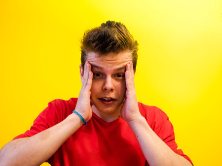  Portrait of a young man with a shocked facial expression isolated on a yellow background