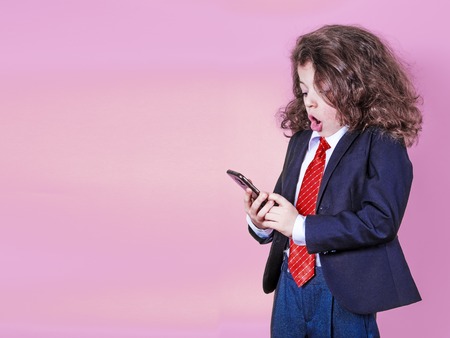 Portrait of a little Caucasian boy holding a two-handed phone with a crazy shocked look and an open mouth in surpriseの写真素材