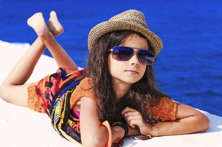A girl in bright clothes and a straw hat lies and rests on the beach on the pierの写真素材