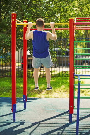 A mature man doing pull-ups at an open gymnastic complex. The concept of a healthy lifestyleの写真素材