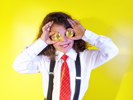 Little boy close his eyes with bitcoin coins on a yellow backgroundの写真素材
