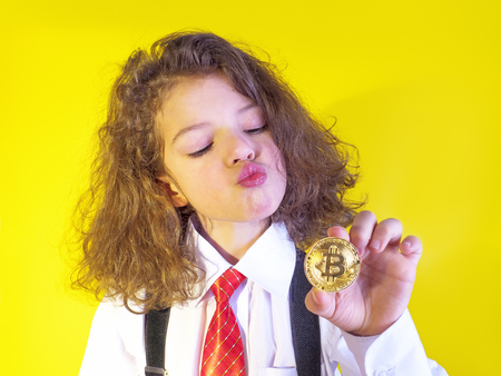 Little funny boy in suit kissing the golden bitcoin in hand, on a yellow backgroundの写真素材