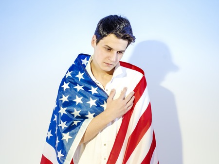 A young handsome man wrapped in a national flag - the United States, laid his hand on his heart. Oath conceptの写真素材