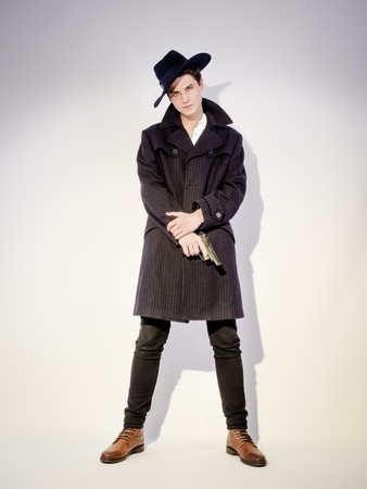 A shot of a young man in a coat with a gun on a light backgroundの写真素材