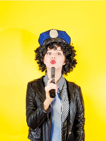 A policewoman is holding up a gun blowing on it, yellow backgrounの写真素材