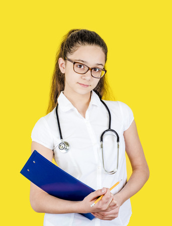 Young girl in doctor's suit with tablet and stethoscope, isolated on yellowの写真素材