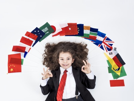 Long-haired boy dressed as a businessman shows a gesture okay lying on the floor on a set of national flags of various statesの写真素材