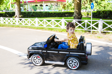 a funny boy rides on a toy electric car on a sunny summer dayの写真素材