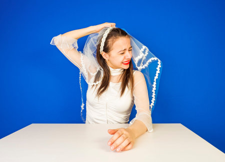 Abandoned bride. Weeps.The charming brunette tears off a veil with a head on a blue background.