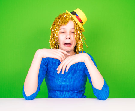 Very unhappy and sad girl with golden haire crying sitting at the table on green background, sequins tearsの写真素材