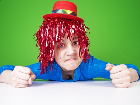 Comedy humorous joke for people. Portrait of a cute restless girl in a wig which grimaces on a green backgroundの写真素材