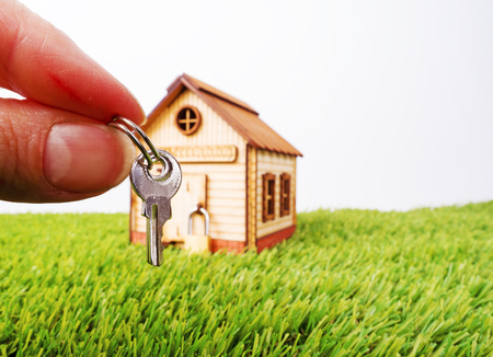 Colorful wooden miniature house green grass, in the foreground hand with a key, new house concept. Selective focusの写真素材