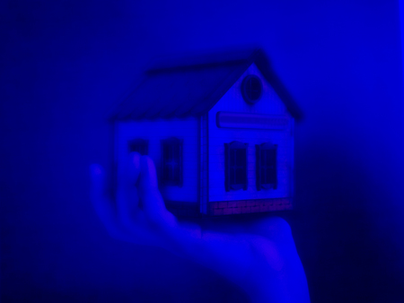 Small toy house in a hand on a dark blue background. The concept of freezing and lifelessnessの写真素材