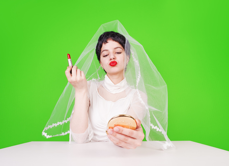 Bride dyes lips. The bride is tidying herself up looking at a small mirror while sitting at a table. Green backgroundの写真素材