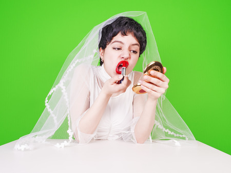 Bride dyes lips. The bride is tidying herself up looking at a small mirror while sitting at a table. Green backgroundの写真素材