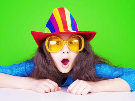 Picture of a young shocked lady wearing a hut sitting at a table isolated over green background. Looking camera.の写真素材