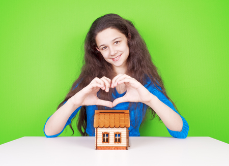Beautiful young woman showing a gesture of the heart with fingers. Portrait of a smiling lady posing with a toy house. The concept of happiness and love.の写真素材