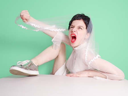 A funny emotional bride put her foot on the table with a sharp cry from an excited stateの写真素材