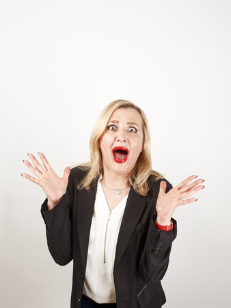Blond female teacher wearing a strict suit keeping hands on head, terrified in panic, joking against a light backgroundの写真素材