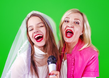 Young Singer bride and her sister with a microphone celebrating her forthcoming mariage. Studio shot. Bright colorful background.の写真素材