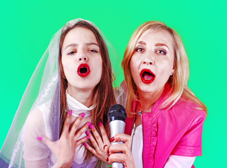 Young Singer bride and her sister with a microphone celebrating her forthcoming mariage. Studio shot. Bright colorful background.の写真素材