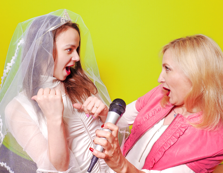 Young Singer bride and her sister with a microphone celebrating her forthcoming mariage. Studio shot. Bright colorful background.の写真素材