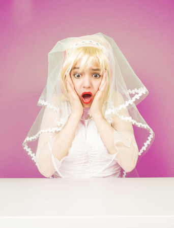 Excited beautiful blonde bride in a white dress on a pink backgroundの写真素材