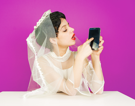 Caucasian bride holding mobile phone and pointing at it. Young bride with a smartphone. Fiancee points her finger, clicks on the black display, an imaginary inscription on the mobile phone.の写真素材