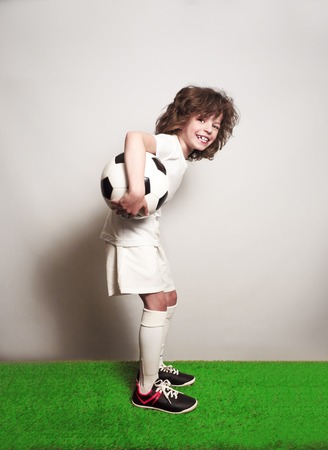 A young football player with a ball is standing on the grass of the stadium.の写真素材