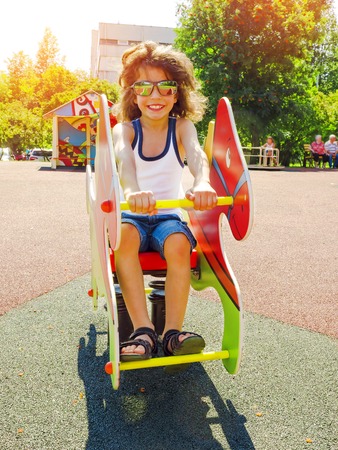 The boy swings on a rocking chair on a spring in the form of a horse. Swings and slides in the park for children. Childrens playground bright colorful. A modern childrens playground for childrenの写真素材